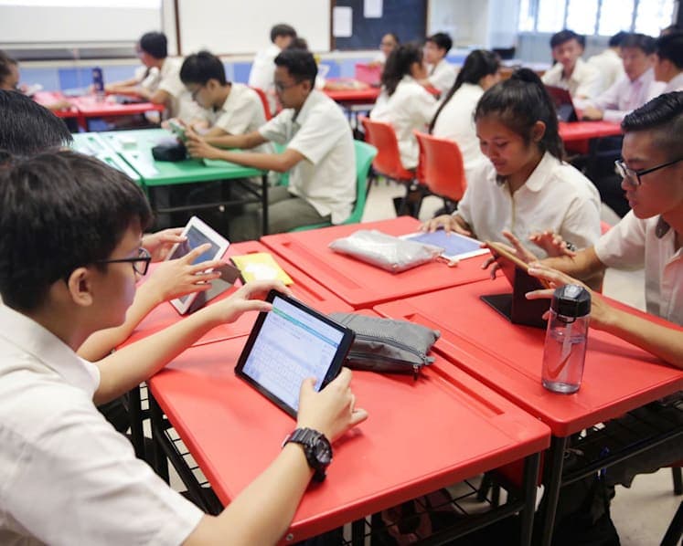 Students using tablets together at their desks in a classroom